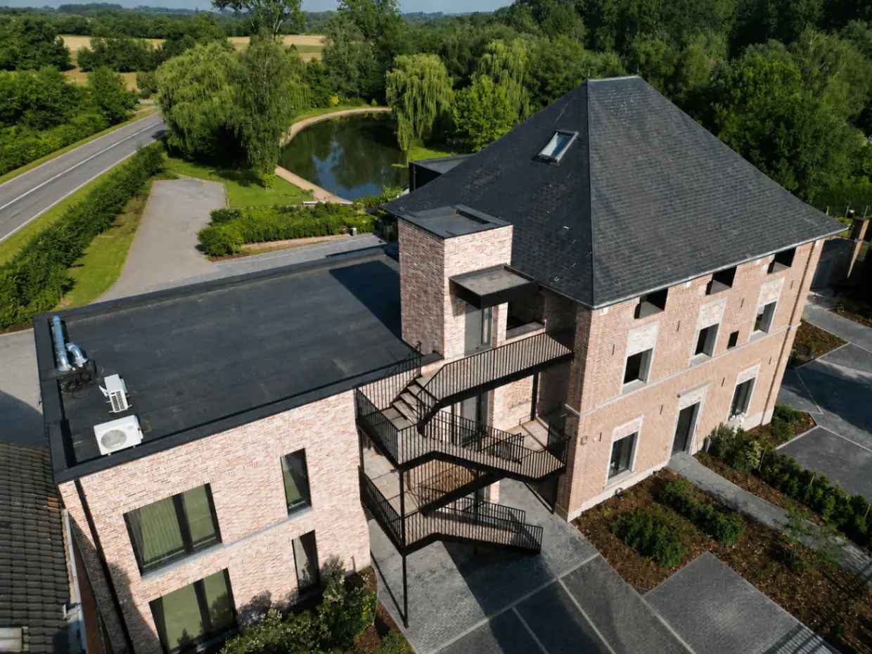Aerial zicht op de achterzijde met buitentrap, loftvolume en vijvercontext van De Castel
